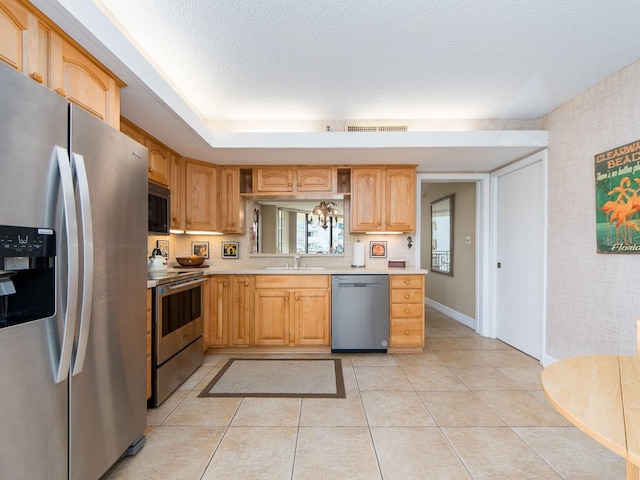 kitchen with light brown cabinetry, sink, a textured ceiling, light tile patterned floors, and stainless steel appliances