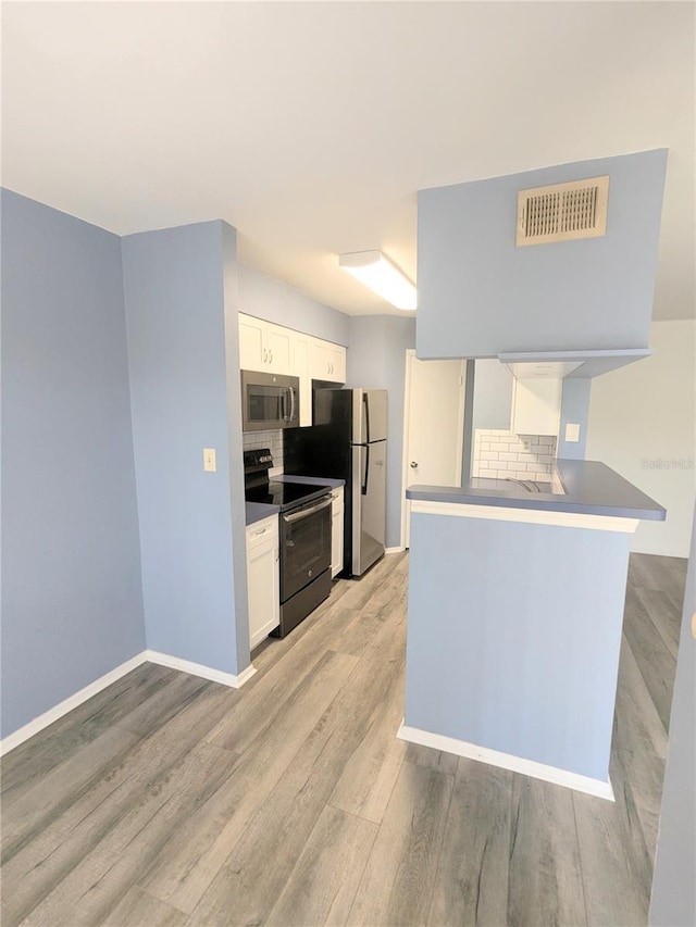 kitchen featuring light hardwood / wood-style floors, kitchen peninsula, appliances with stainless steel finishes, tasteful backsplash, and white cabinets