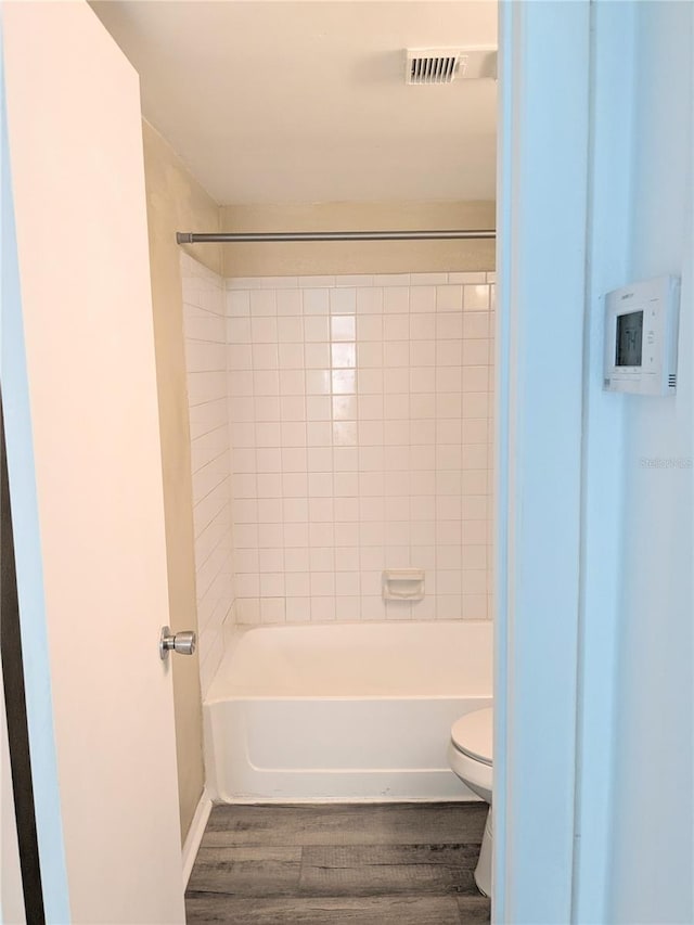 bathroom with hardwood / wood-style floors, toilet, and tiled shower / bath combo