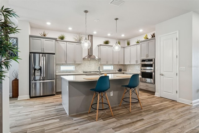 kitchen featuring appliances with stainless steel finishes, gray cabinets, hanging light fixtures, and wall chimney range hood