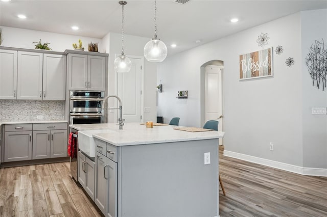 kitchen with gray cabinets, a kitchen island with sink, and decorative backsplash