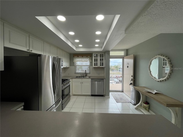 kitchen featuring a raised ceiling, white cabinetry, sink, light tile patterned floors, and stainless steel appliances