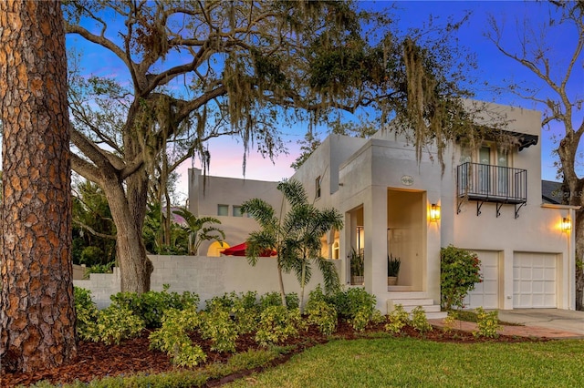 view of front of property with stucco siding, concrete driveway, fence, a balcony, and a garage