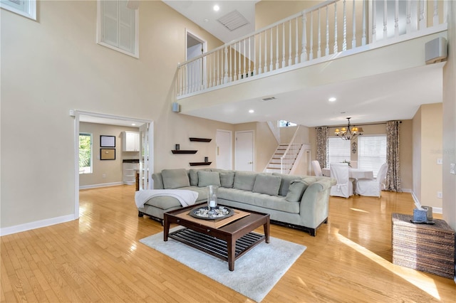 living room with light wood-type flooring, a chandelier, a healthy amount of sunlight, and a towering ceiling