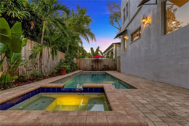 pool at dusk with an in ground hot tub