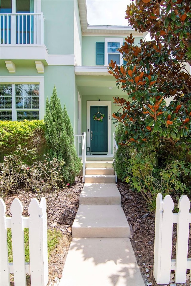 entrance to property with a balcony, fence, and stucco siding