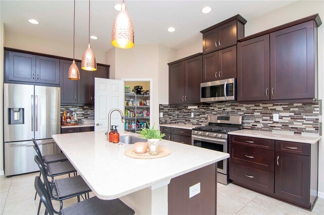 kitchen featuring stainless steel appliances, light countertops, a sink, dark brown cabinets, and a kitchen bar