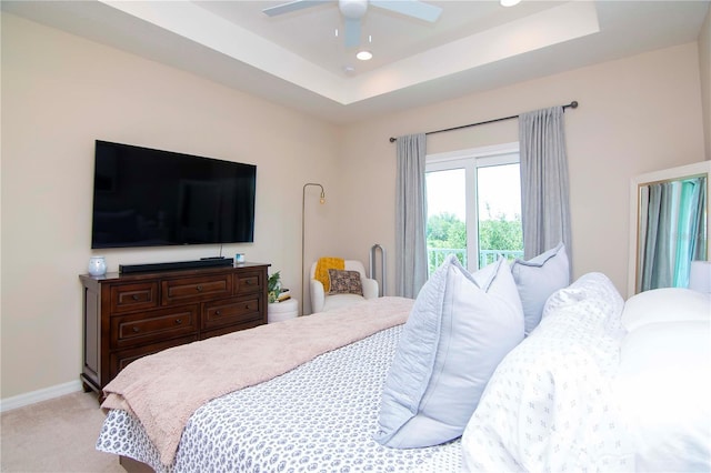 bedroom featuring light carpet, baseboards, a raised ceiling, and a ceiling fan