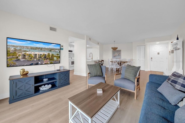 living room with visible vents, light wood-style flooring, and baseboards