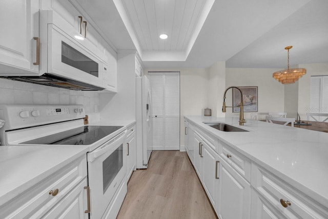 kitchen with light wood-style flooring, white appliances, a sink, decorative backsplash, and a tray ceiling