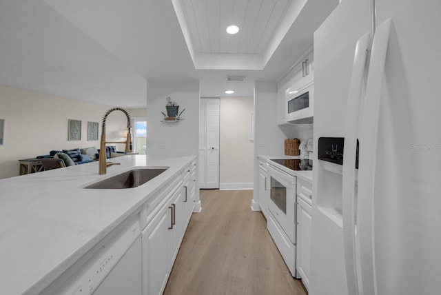 kitchen featuring a raised ceiling, light wood-style flooring, white cabinets, a sink, and white appliances