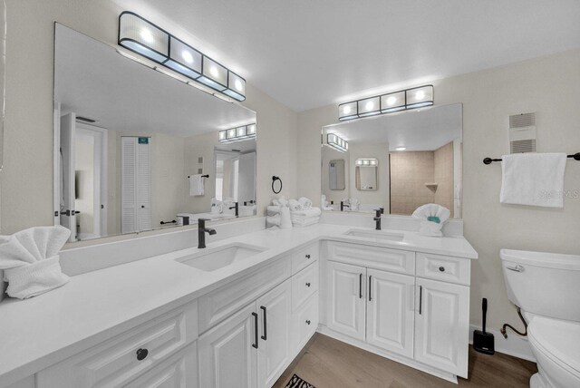 full bathroom featuring double vanity, wood finished floors, a sink, and toilet