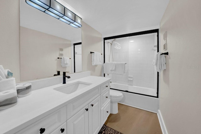 bathroom with toilet, wood finished floors, vanity, and enclosed tub / shower combo