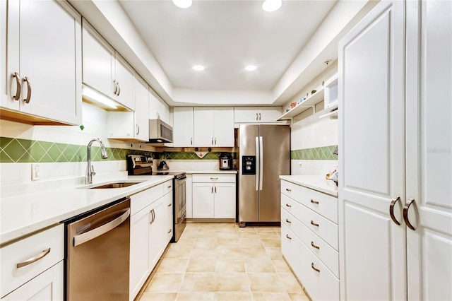 kitchen featuring a tray ceiling, sink, white cabinetry, and appliances with stainless steel finishes