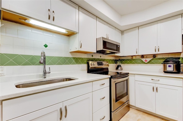 kitchen featuring tasteful backsplash, sink, light tile patterned flooring, appliances with stainless steel finishes, and white cabinets