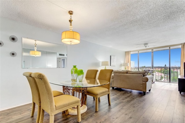 dining room featuring ceiling fan, a wall of windows, wood-type flooring, and a textured ceiling