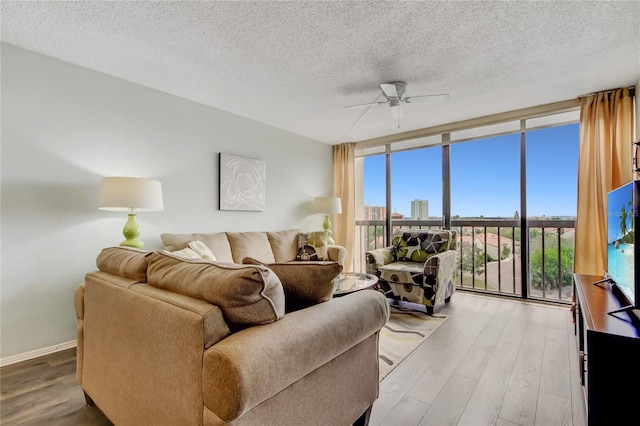 living room featuring ceiling fan, hardwood / wood-style floors, a wall of windows, and a textured ceiling