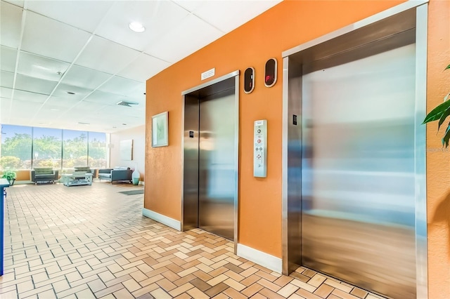 hallway with a wall of windows, a paneled ceiling, and elevator