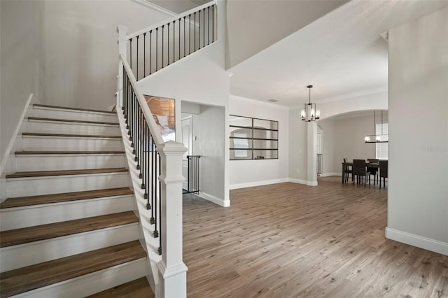 stairway with a chandelier, wood-type flooring, and ornamental molding