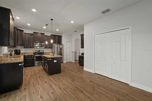 kitchen with appliances with stainless steel finishes, a center island, sink, hanging light fixtures, and light wood-type flooring