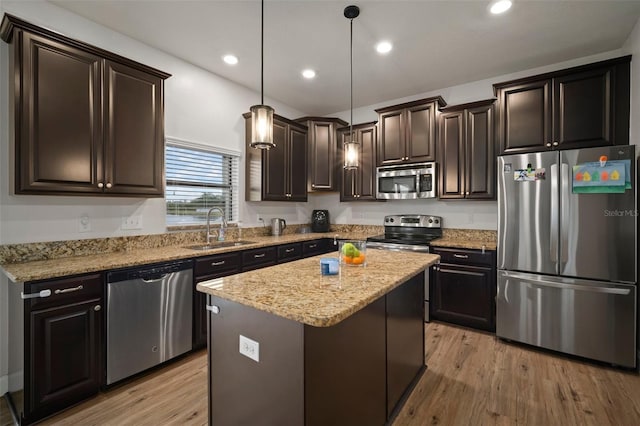 kitchen featuring decorative light fixtures, light hardwood / wood-style floors, a center island, sink, and appliances with stainless steel finishes