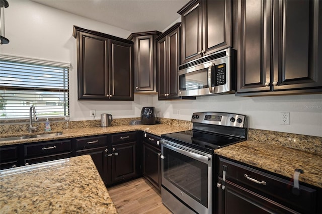 kitchen with stainless steel appliances, sink, light stone counters, light hardwood / wood-style flooring, and dark brown cabinets