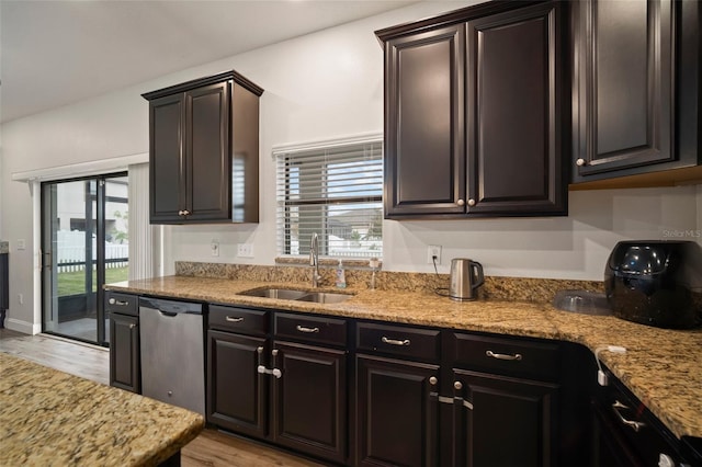 kitchen featuring light wood-type flooring, dark brown cabinets, stainless steel dishwasher, light stone counters, and sink