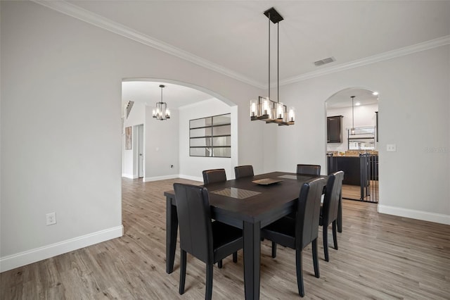 dining room with a notable chandelier, crown molding, and light hardwood / wood-style flooring