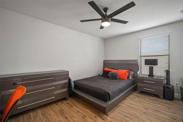 bedroom with ceiling fan, light wood-type flooring, and a textured ceiling