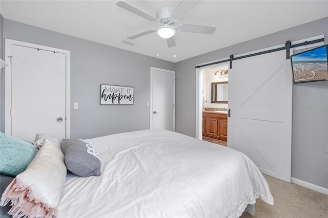 bedroom with ensuite bathroom, a barn door, carpet flooring, and ceiling fan