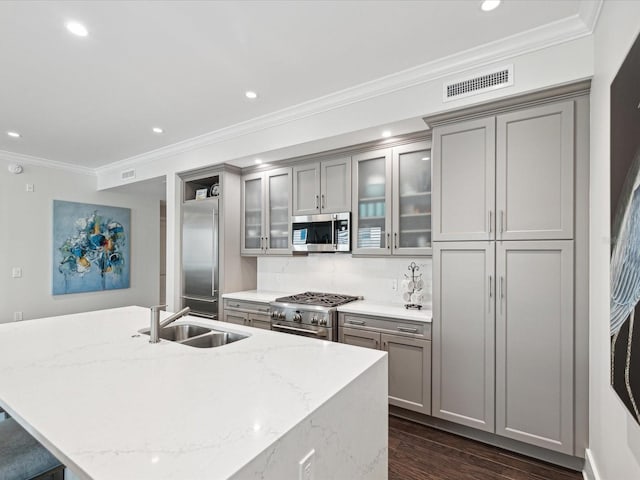 kitchen featuring high end appliances, sink, light stone counters, and gray cabinetry