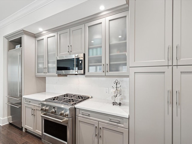 kitchen with gray cabinetry, high end appliances, ornamental molding, dark hardwood / wood-style flooring, and light stone countertops