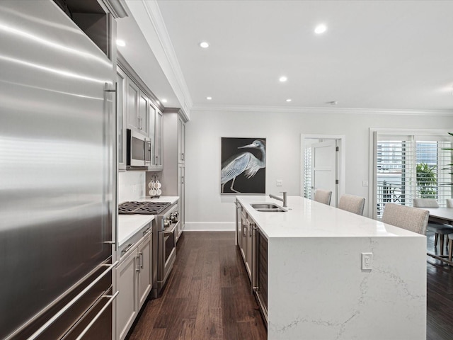 kitchen featuring high quality appliances, sink, ornamental molding, light stone countertops, and a center island with sink