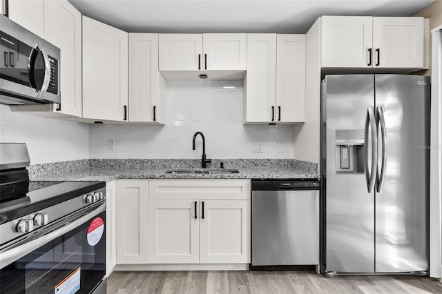 kitchen with appliances with stainless steel finishes, sink, white cabinets, light stone counters, and decorative backsplash