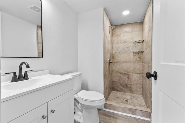 bathroom featuring hardwood / wood-style flooring, toilet, tiled shower, and vanity