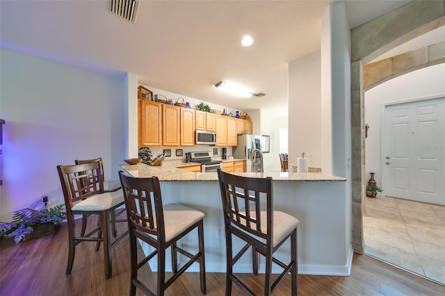 kitchen with kitchen peninsula, light hardwood / wood-style flooring, light stone countertops, appliances with stainless steel finishes, and a breakfast bar area