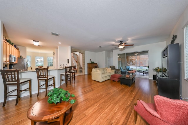 living room with ceiling fan with notable chandelier, a textured ceiling, and light wood-type flooring