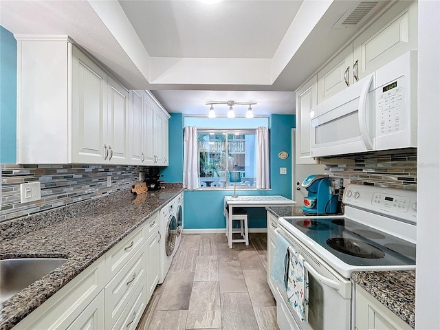 kitchen featuring washer / dryer, white appliances, white cabinets, dark stone counters, and rail lighting