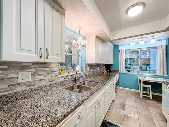 kitchen featuring white cabinets, dark stone counters, sink, backsplash, and hanging light fixtures