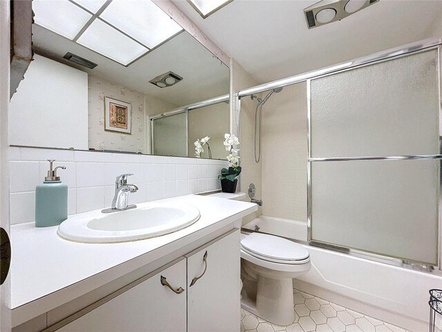 full bathroom featuring tasteful backsplash, bath / shower combo with glass door, vanity, toilet, and tile patterned floors