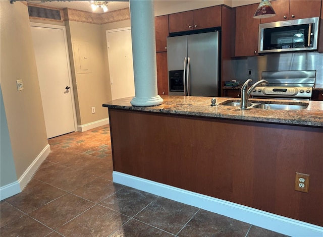 kitchen with sink, decorative columns, stainless steel appliances, kitchen peninsula, and dark stone counters