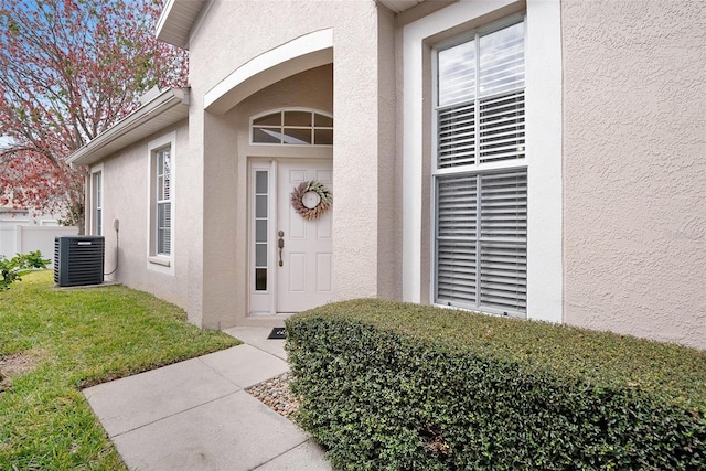 property entrance featuring central air condition unit, a yard, and stucco siding