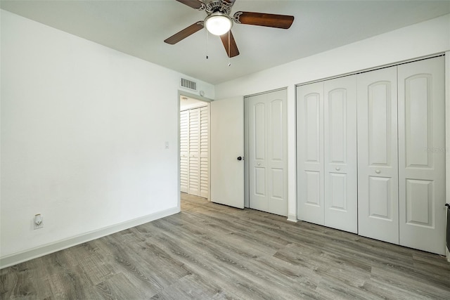 unfurnished bedroom featuring ceiling fan, light hardwood / wood-style floors, and two closets