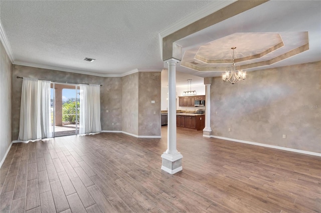 unfurnished living room featuring a raised ceiling, ornate columns, hardwood / wood-style flooring, a textured ceiling, and an inviting chandelier