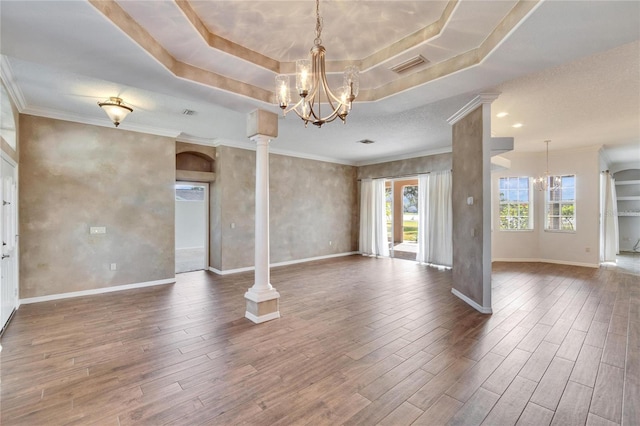 empty room featuring a notable chandelier, decorative columns, and a tray ceiling