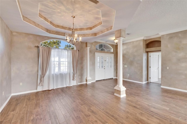 interior space with a raised ceiling, ornate columns, crown molding, and wood-type flooring