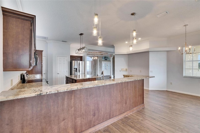 kitchen with stainless steel fridge with ice dispenser, hanging light fixtures, an inviting chandelier, and light stone countertops