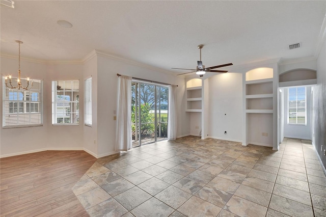 unfurnished living room featuring built in shelves, ceiling fan with notable chandelier, a healthy amount of sunlight, and crown molding