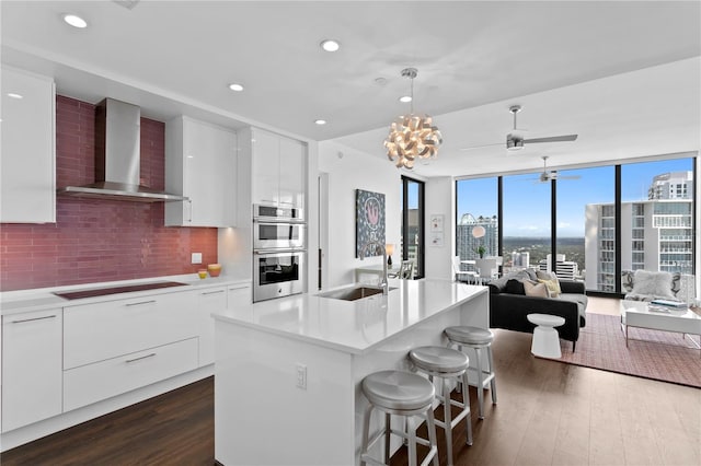 kitchen featuring wall chimney range hood, decorative backsplash, sink, stovetop, and white cabinets