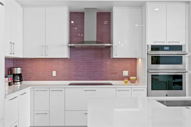 kitchen with white cabinetry, decorative backsplash, black stovetop, wall chimney exhaust hood, and double oven